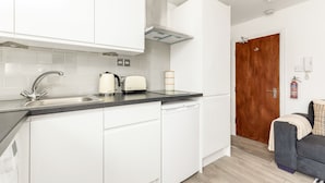 A modern kitchen with white cabinets, a stainless steel sink, and a toaster. - The Paddington Rooms (London)