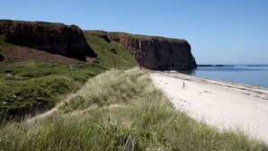 A coastal landscape with a sandy beach, grassy dunes, and a cliff. - Hotel Klippenklang (Helgoland)