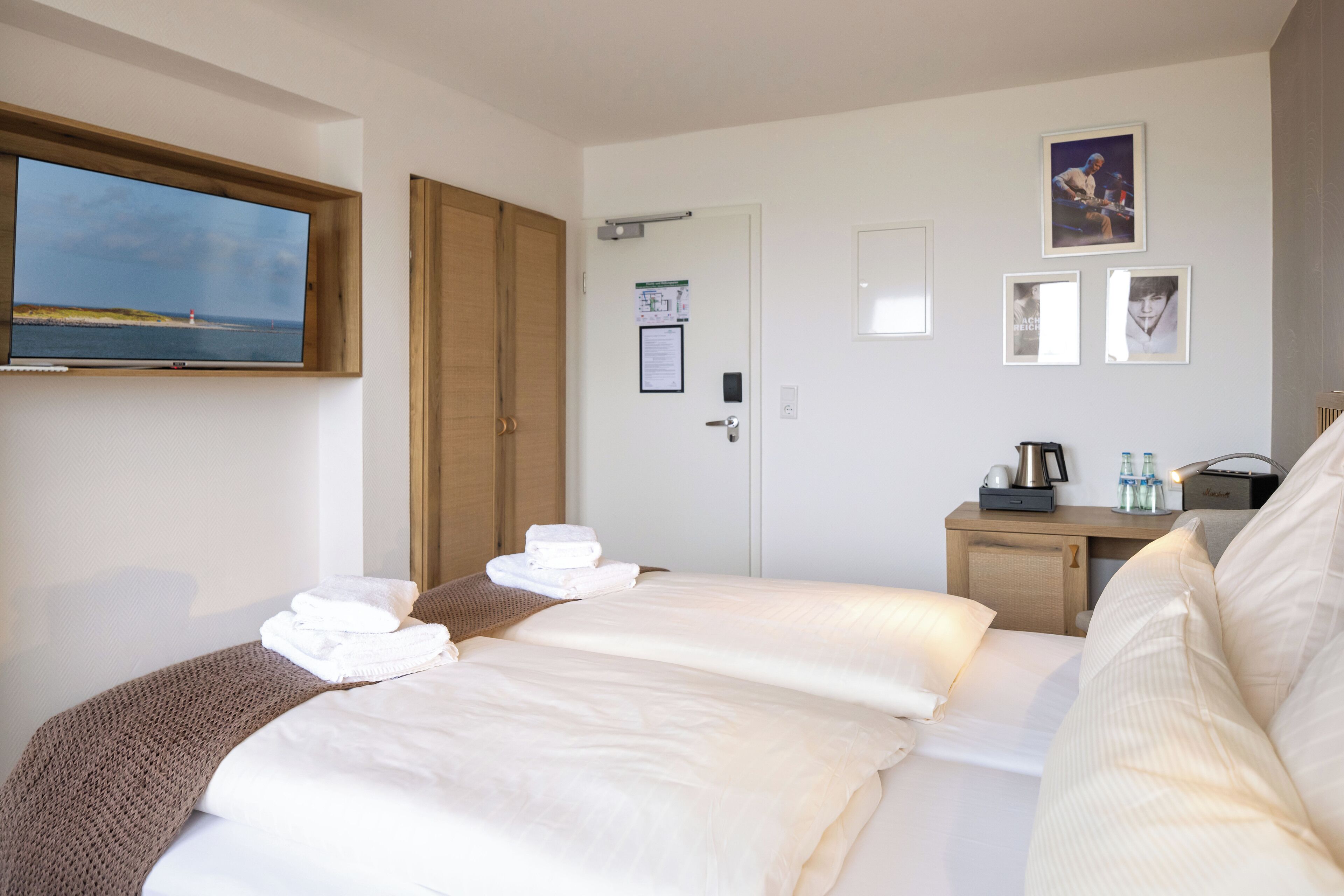 Une chambre d’hôtel comprenant un lit, un téléviseur fixé au mur, une porte et une petite table avec une bouilloire et des tasses.
