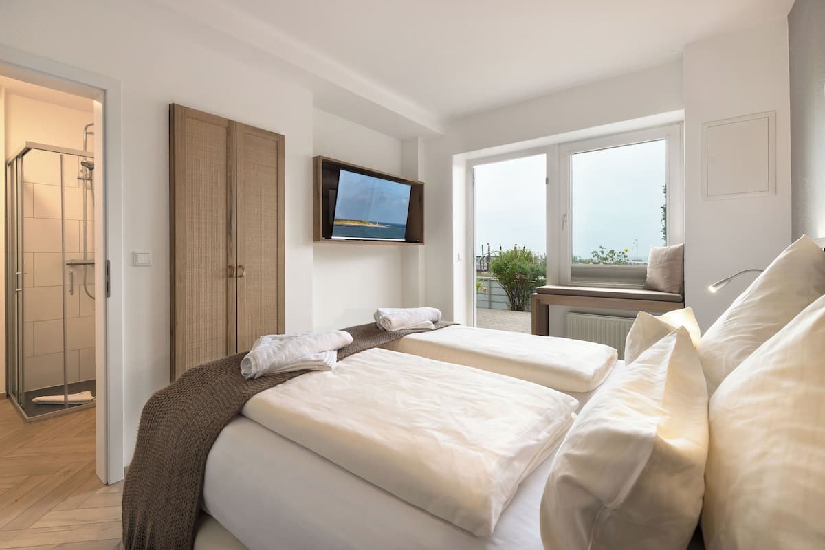 A hotel room with two beds, a TV, a shower, and a balcony with a view.