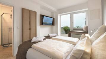 A hotel room with two beds, a TV, a shower, and a balcony with a view.