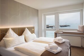 Una habitación de hotel moderna con una cama grande, un banco junto a la ventana y vistas al mar.