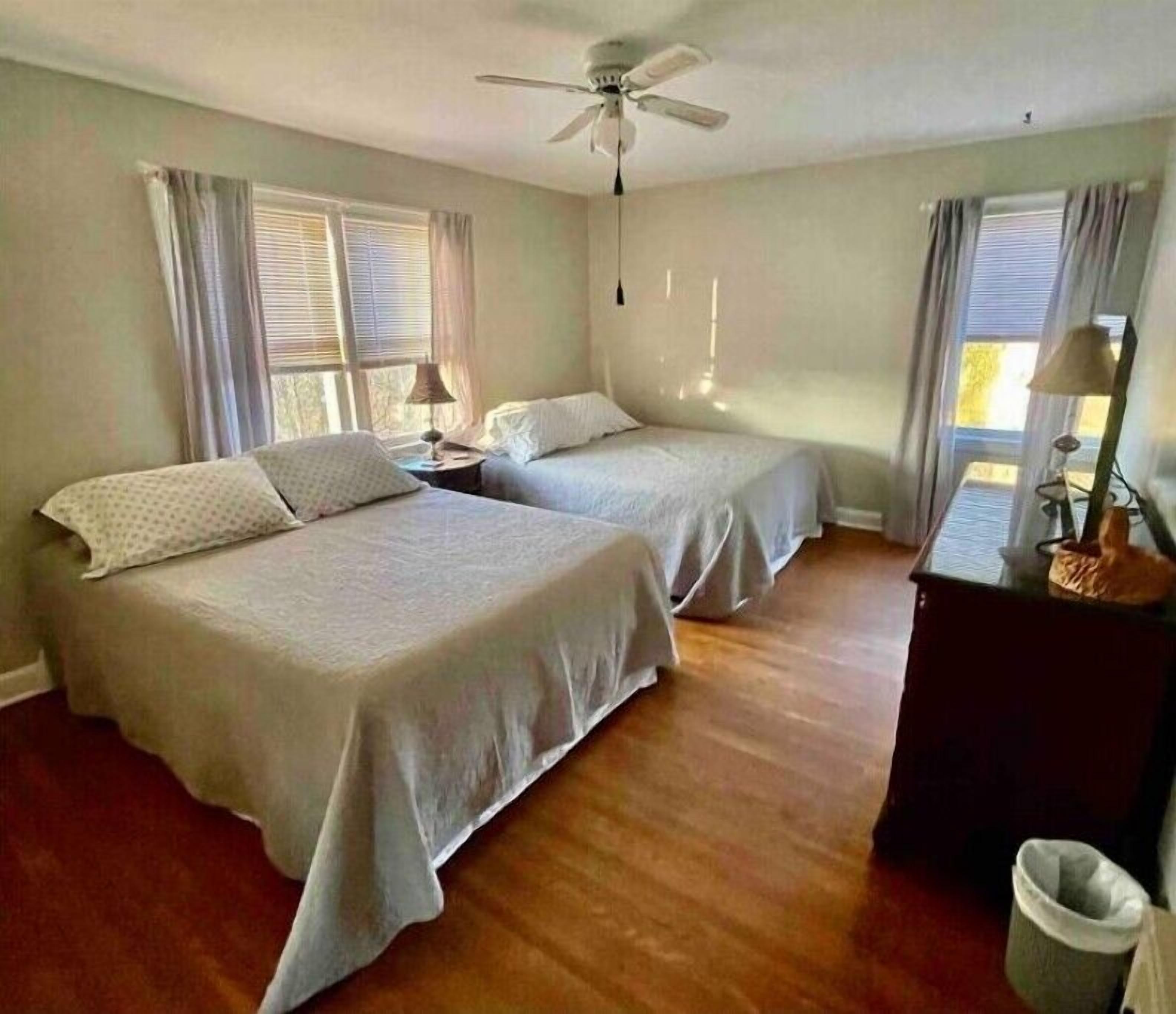 A room with two beds, a ceiling fan, and a window with curtains.