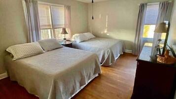 A room with two beds, a ceiling fan, and a window with curtains.
