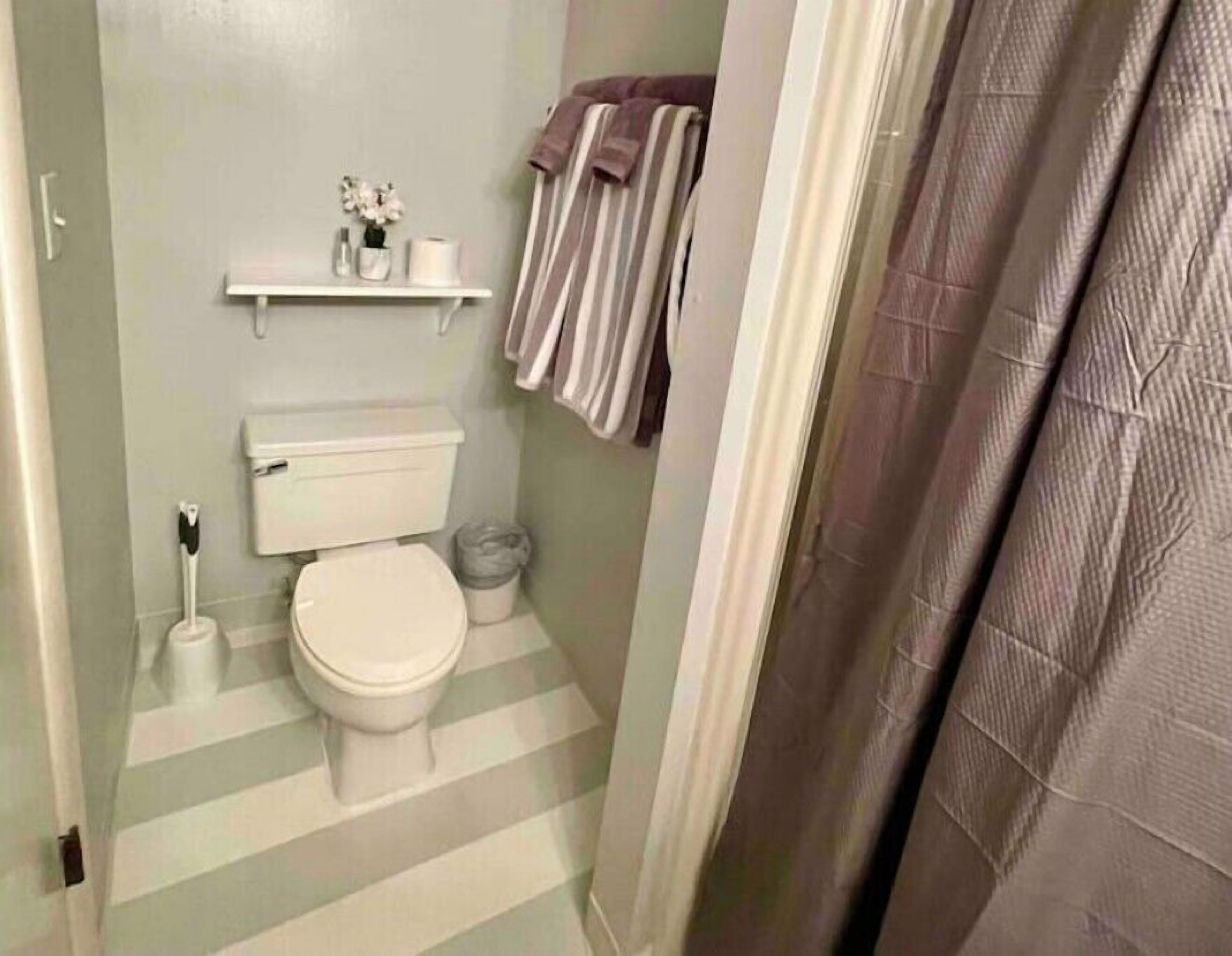 Une salle de bain avec des toilettes, une étagère contenant des articles de toilette et un sol à rayures.
