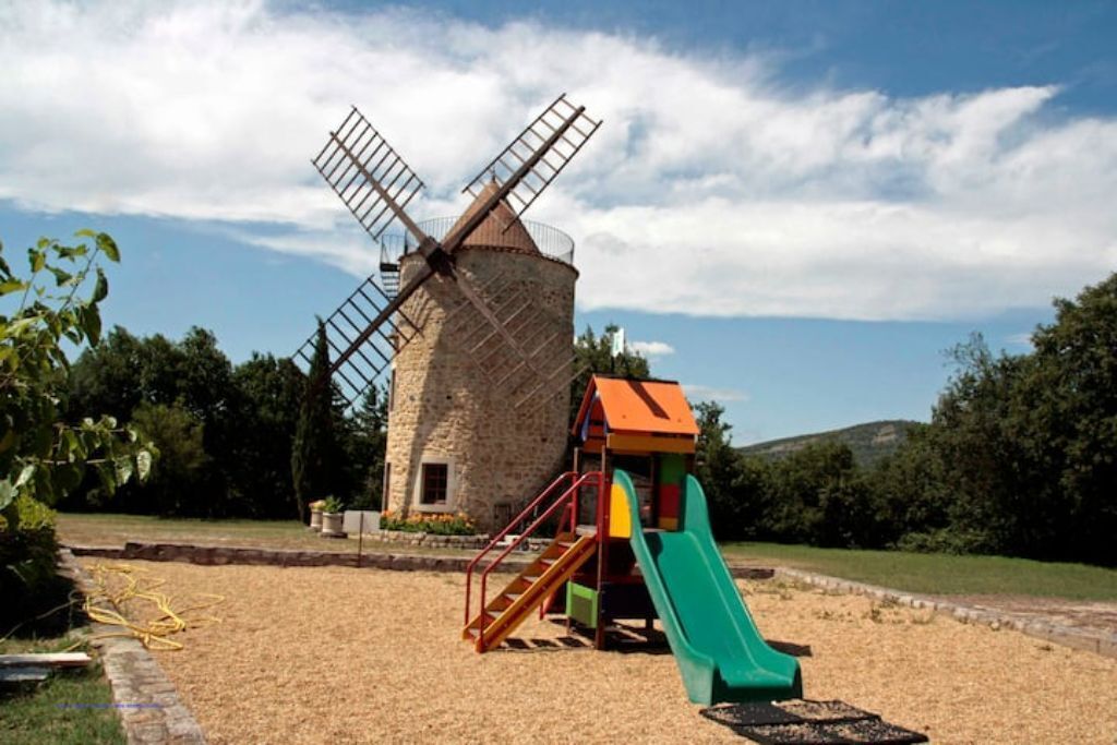 Un parque infantil con un tobogán y un molino de viento al fondo.