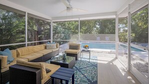 A sunlit patio with a pool, wicker furniture, and a ceiling fan.