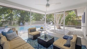 A sunlit indoor patio with a pool, outdoor furniture, and large windows.