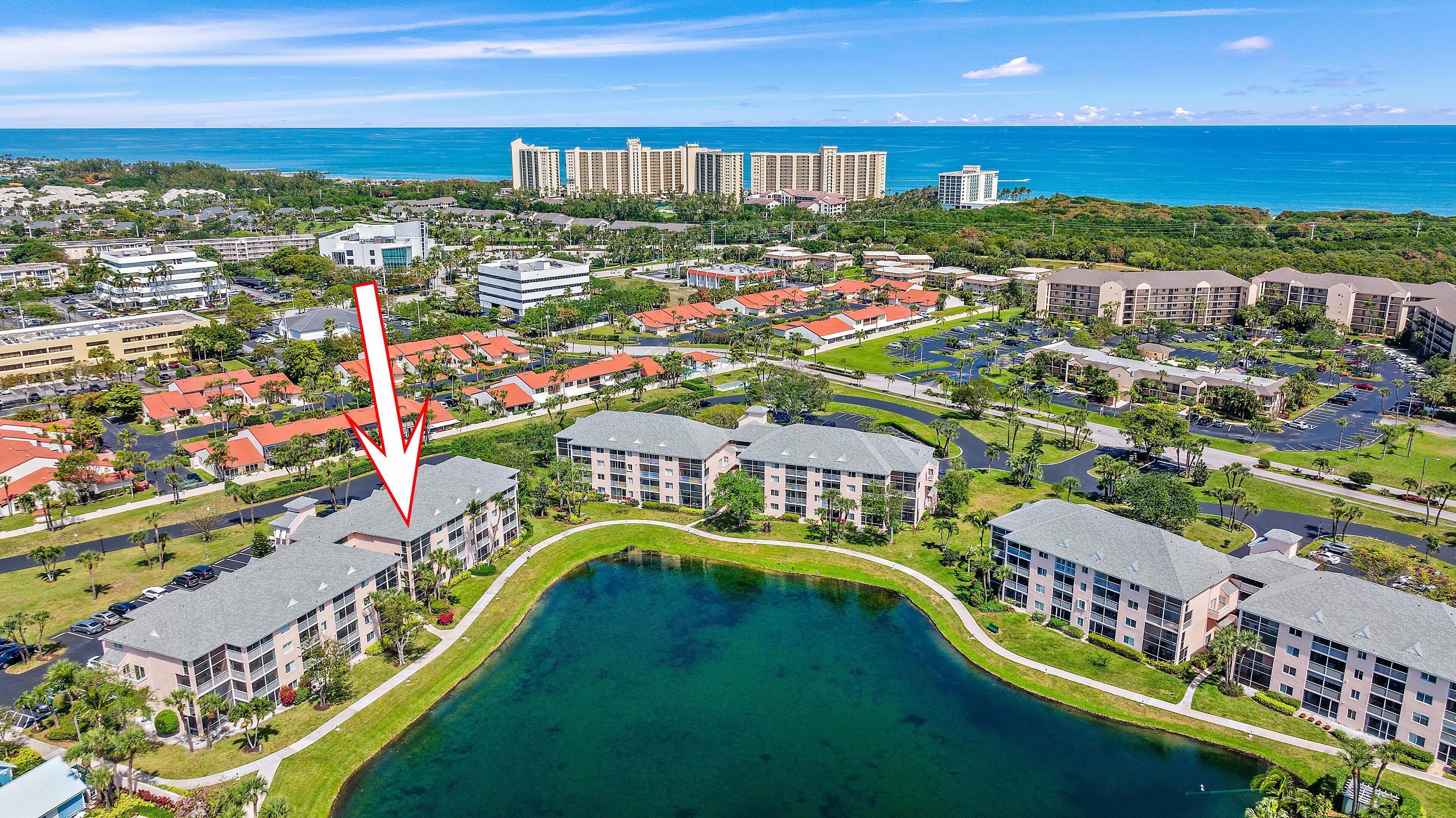 An aerial view of a resort with multiple buildings, a central water feature, and a view of the ocean.