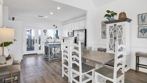 Une cuisine moderne avec des meubles blancs, une table à manger en bois et un coin salon avec des chaises blanches.