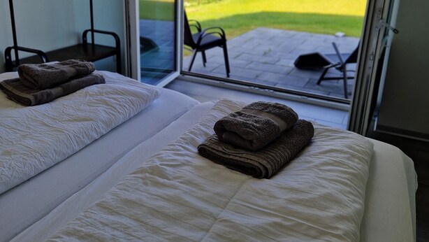 Quarto de hotel com duas camas, uma janela grande e vista para uma área gramada.