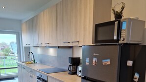Cozinha moderna com armários de madeira clara, geladeira de aço inoxidável, micro-ondas e cafeteira.