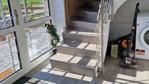 Interior moderno com uma escadaria que leva a um segundo andar, uma máquina de lavar e vista para uma paisagem verde através de uma grande janela.
