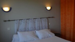 A bedroom with a bed, two wall-mounted lights, and a curtain with a wavy pattern. - Maison Entre Rivière et Village (Vallon-Pont-d'Arc)