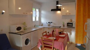 A compact kitchen with a washing machine, microwave, and a dining area with a table set for two. - Maison Entre Rivière et Village (Vallon-Pont-d'Arc)