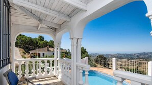 Ein überdachter Außenbereich mit Pool, weißen Brüstungen und Blick auf die Landschaft.