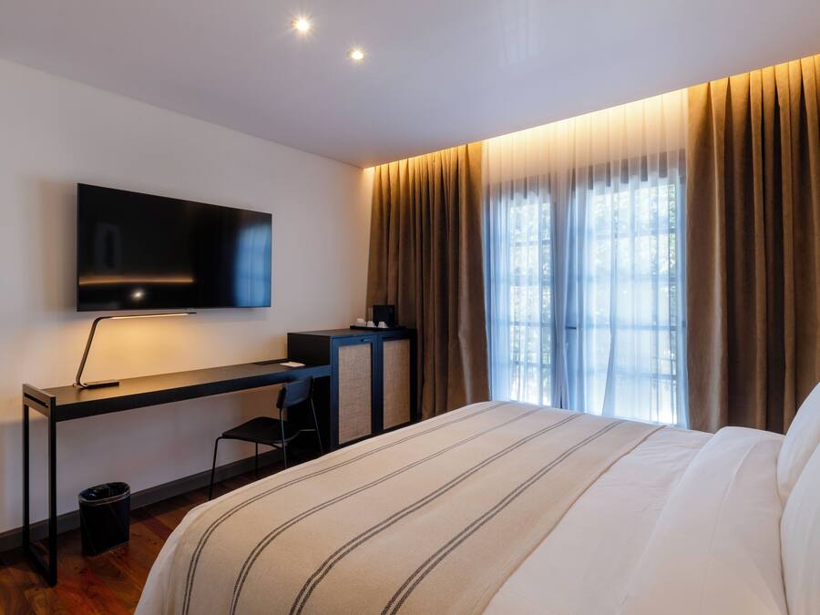 Habitación de hotel moderna con una cama grande, un escritorio con televisor de pantalla plana y una ventana con cortinas.