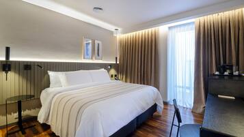 A hotel room with a large bed, a desk with a coffee machine, a chair, and a window with curtains.