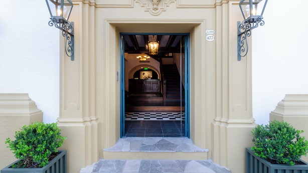 Entrada de un edificio con suelo de ajedrez, una escalera y dos faroles en las paredes.