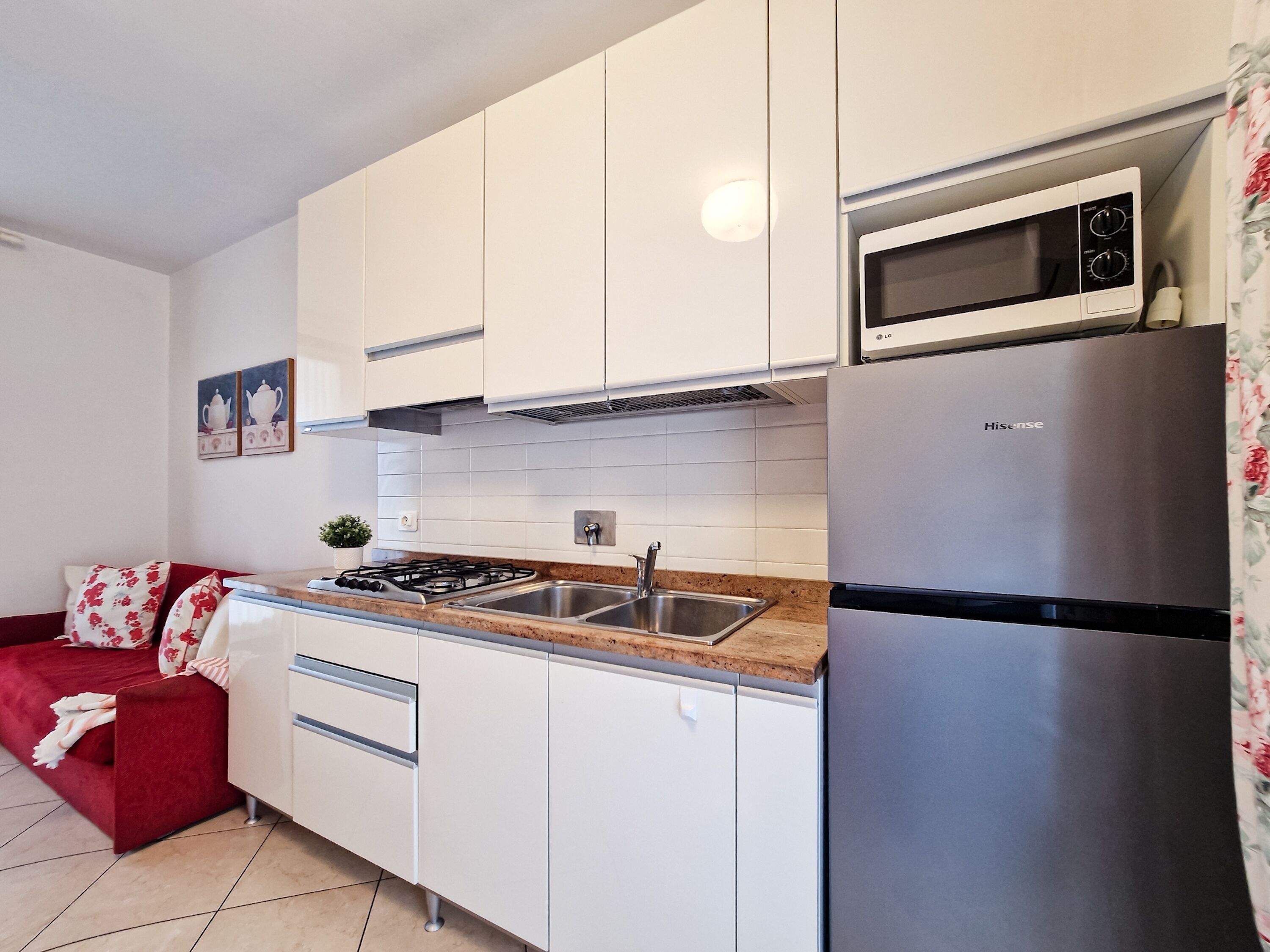 Una cucina compatta con mobili bianchi, un frigorifero in acciaio inossidabile, un forno a microonde e un piano cottura a gas.