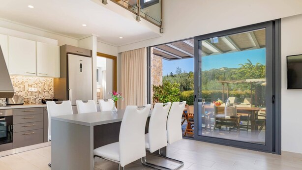 A modern kitchen with white cabinets, a dining area with white chairs, and a large sliding glass door leading to an outdoor patio.