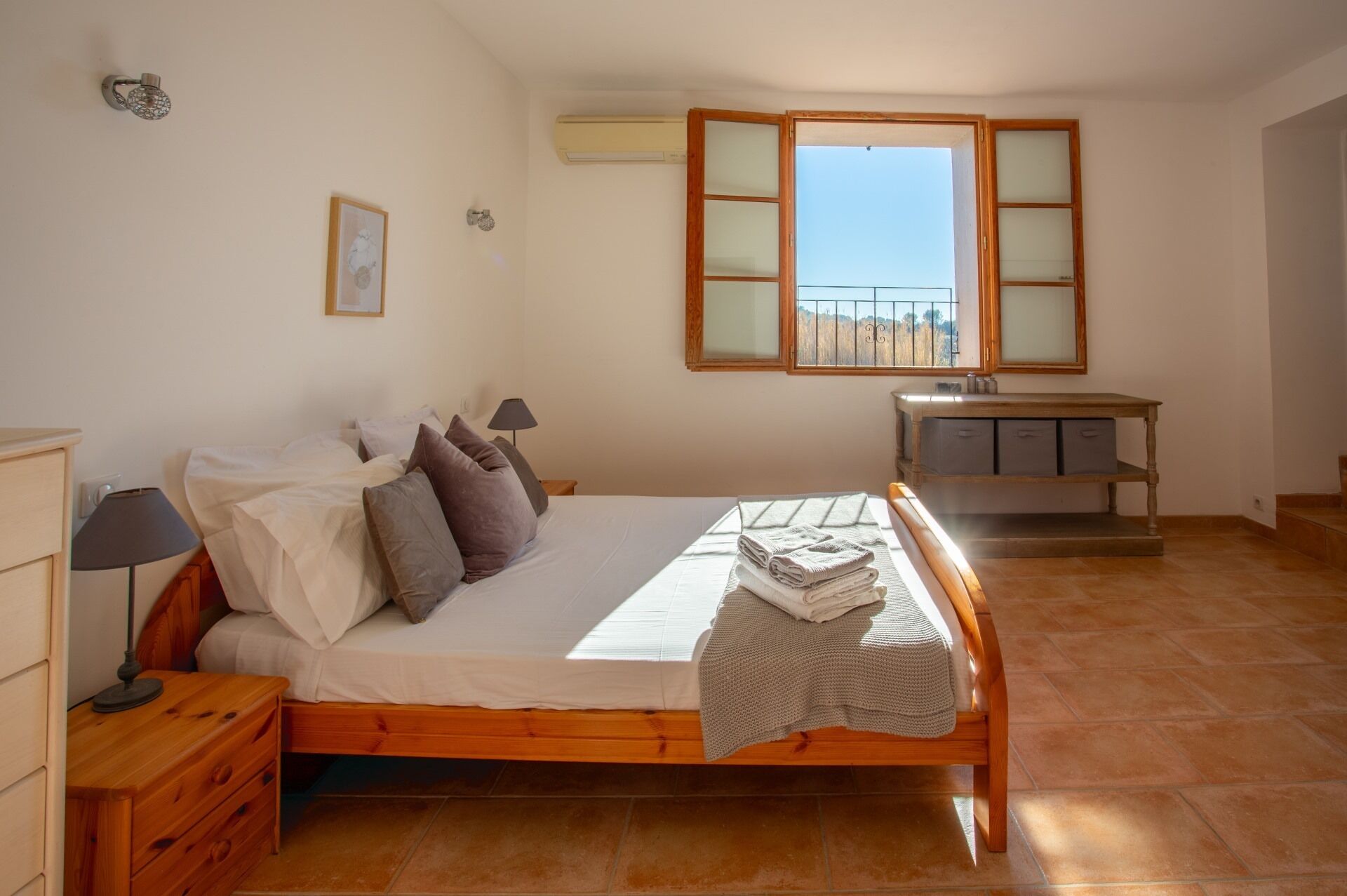 Un dormitorio con cama de madera, mesita de noche, cómoda, escritorio con cajones, ventana con vistas y aire acondicionado instalado en la pared.