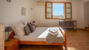 A bedroom with a wooden bed, a nightstand, a dresser, a desk with drawers, a window with a view, and a wall-mounted air conditioner. - Villa Les Juliannes by Villa Plus (Azillanet)