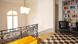 Une pièce avec un sol à carreaux, une bibliothèque remplie de livres, un fauteuil en cuir noir et un canapé jaune.