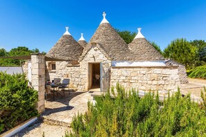 A stone house with conical roofs and a small patio area with outdoor seating. - Villa Trullo Selva Grande by Villa Plus (Martina Franca)