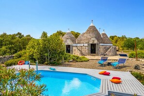 Un espace piscine avec des chaises longues et un petit bâtiment en pierre doté de toits coniques.