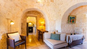 Une pièce chaleureuse aux murs de pierre, avec un canapé, un fauteuil et une petite table sur laquelle se trouve une lampe.