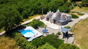 Vue aérienne d’une propriété dotée d’une piscine, d’un bâtiment en pierre surmonté de toits coniques et entourée de verdure.