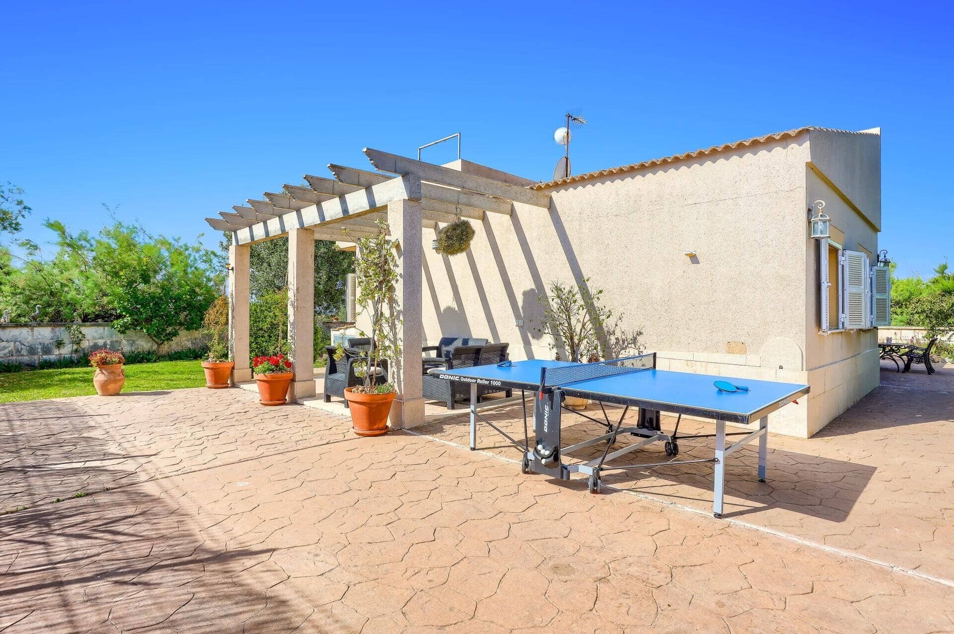 An outdoor ping pong table set up in a courtyard with potted plants and a pergola structure.