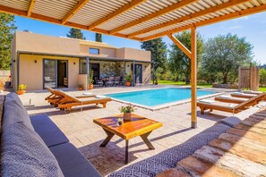 Ein moderner Poolbereich im Freien mit Liegestühlen, einem Holztisch und einer überdachten Lounge-Ecke.