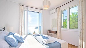 Une chambre d’hôtel équipée d’un lit, d’un bureau, d’un miroir et de grandes fenêtres donnant sur la mer.