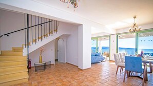 Un intérieur spacieux avec un escalier, un coin repas offrant une vue dégagée et un balcon donnant sur la mer.