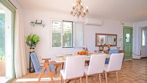 Un coin repas avec une table dressée pour quatre personnes, entourée de chaises, d’un lustre et d’une grande fenêtre donnant sur un paysage verdoyant.