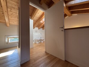 A room with wooden flooring, a sloped ceiling, and a door leading to a bathroom with a toilet and bidet.