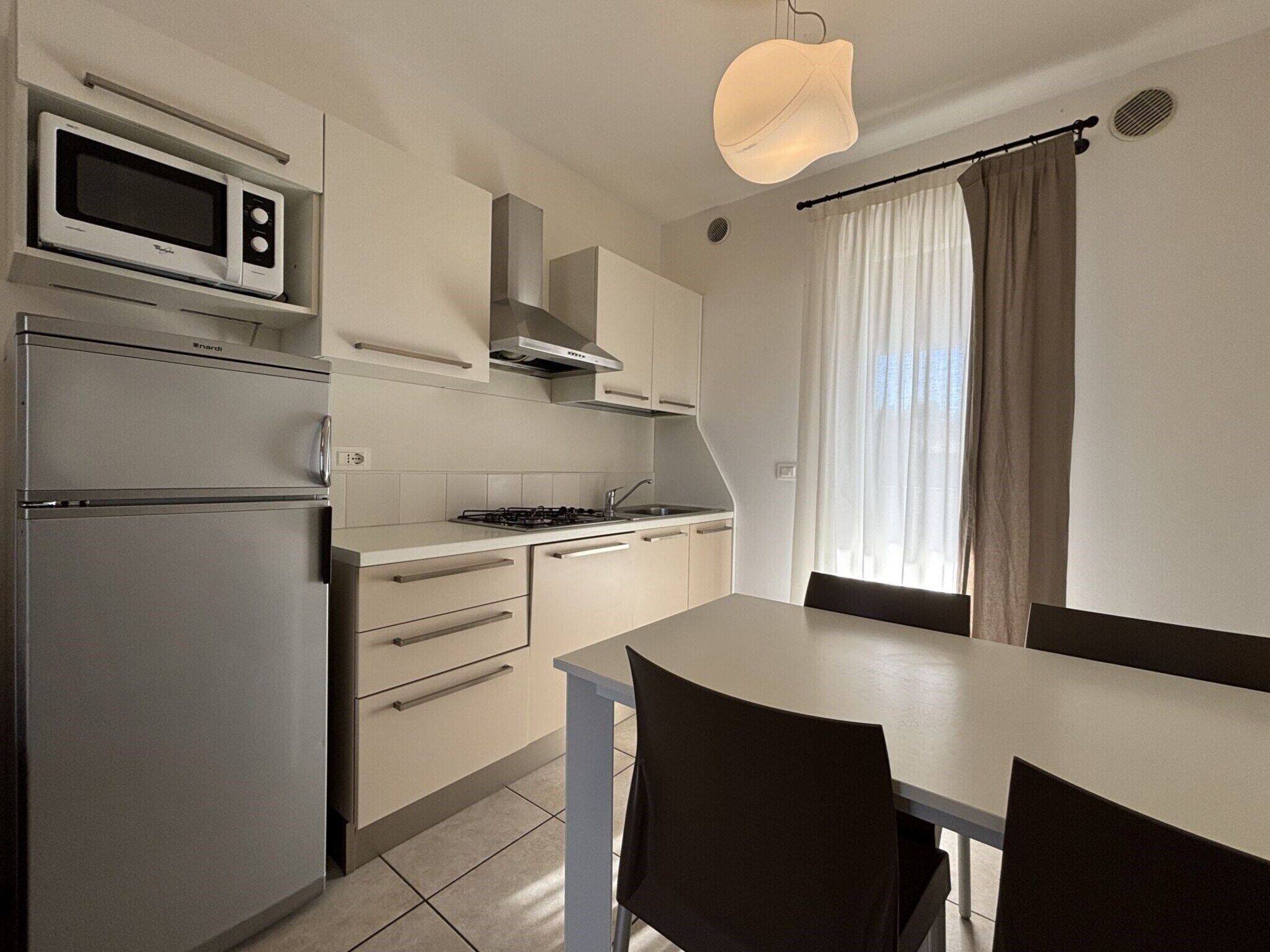 A compact kitchen with a built-in microwave, stove, and oven. There is a dining table with chairs and a pendant light above.