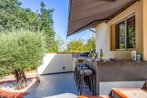 An outdoor bar area with a counter, stools, and a view of the surrounding greenery.