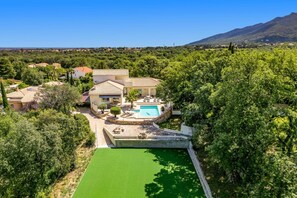 Una villa con piscina rodeada de exuberante vegetación y una montaña al fondo.