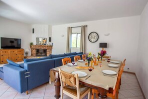 Una sala de estar moderna con un sofá seccional azul, una mesa de comedor lista para cuatro comensales y una chimenea.