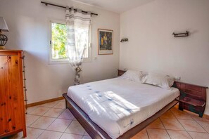 A bedroom with a bed, a window with curtains, a painting on the wall, and a wooden cabinet.
