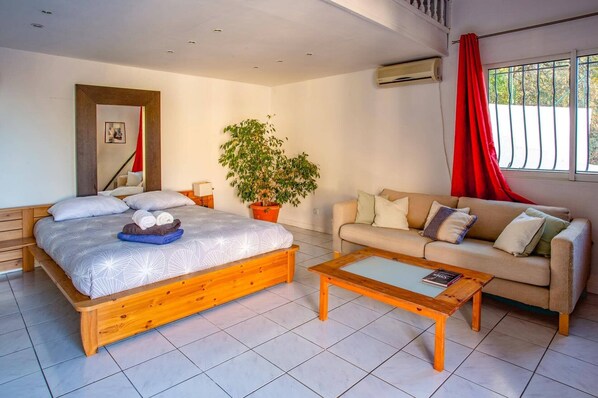 A modern bedroom with a bed, a sofa, a coffee table, and a potted plant.