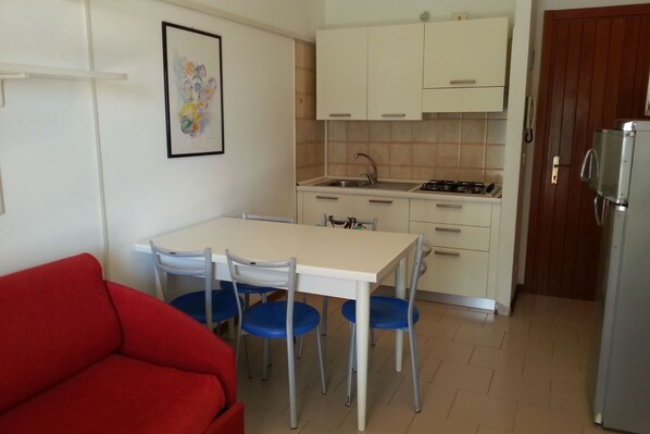 Une cuisine de taille réduite comprenant une table à manger, des chaises, un canapé rouge et un réfrigérateur.