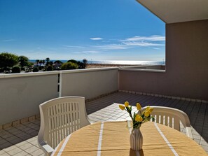 Ein Balkon mit Tisch und Stühlen, eine Vase mit gelben Blumen und Blick aufs Meer.