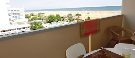 A balcony with a view of a beach, a table with a placemat, and a chair.
