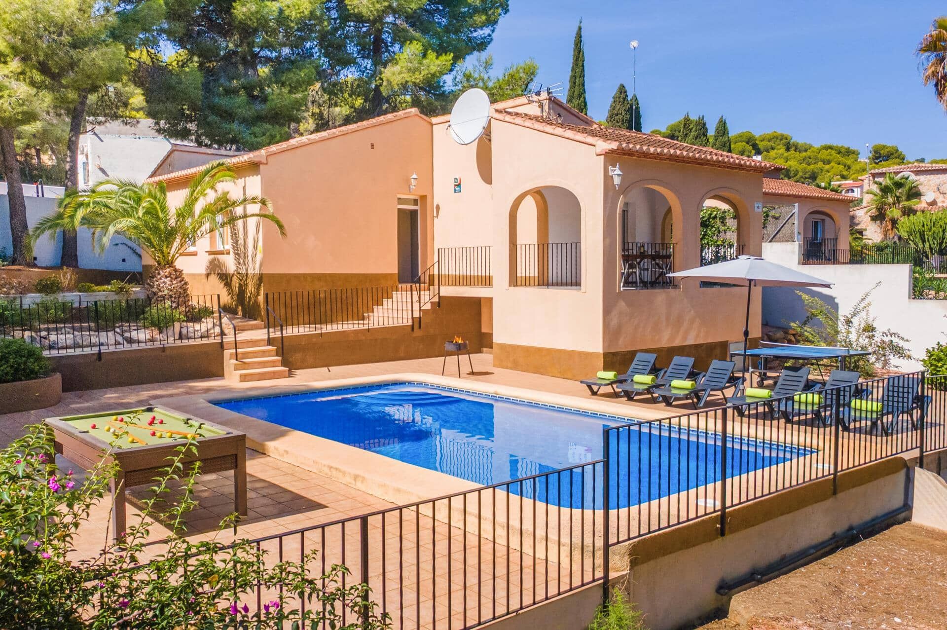 A pool area with a rectangular pool, sun loungers, a table with a pool table, and a small outdoor grill.