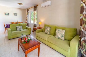A living room with a green sofa, a wooden coffee table with a floral arrangement, and a dining area with a table and chairs. - Villa Encina by Villa Plus (Teulada)