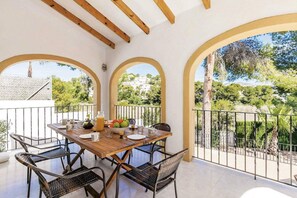 A dining area with a wooden table and chairs, surrounded by arched white walls and a balcony with a metal railing. - Villa Encina by Villa Plus (Teulada)